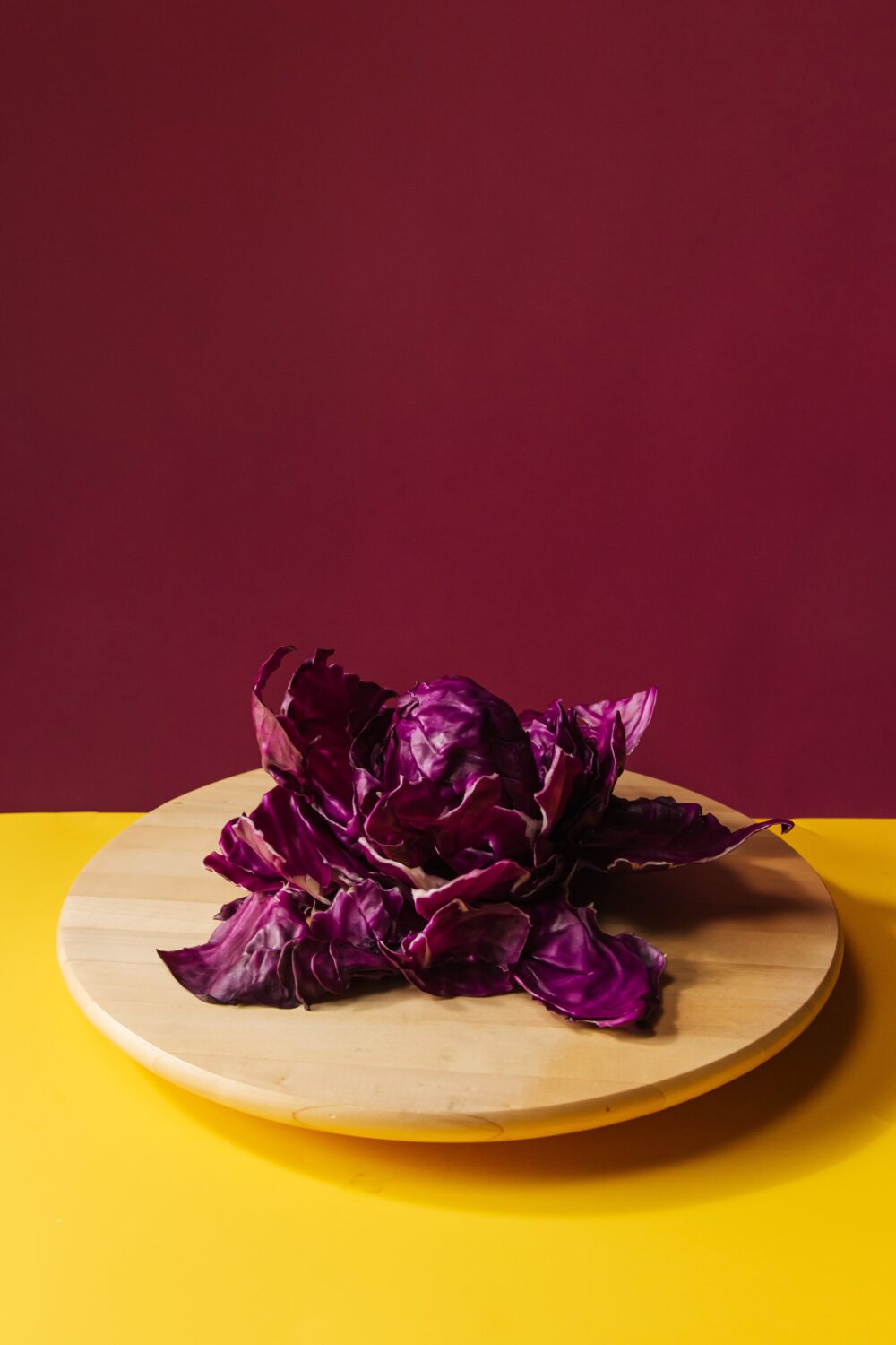Purple cabbage on wooden board, yellow and burgundy background.