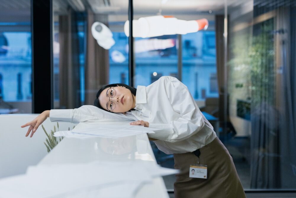 Person in office leans on desk, appearing tired or bored.