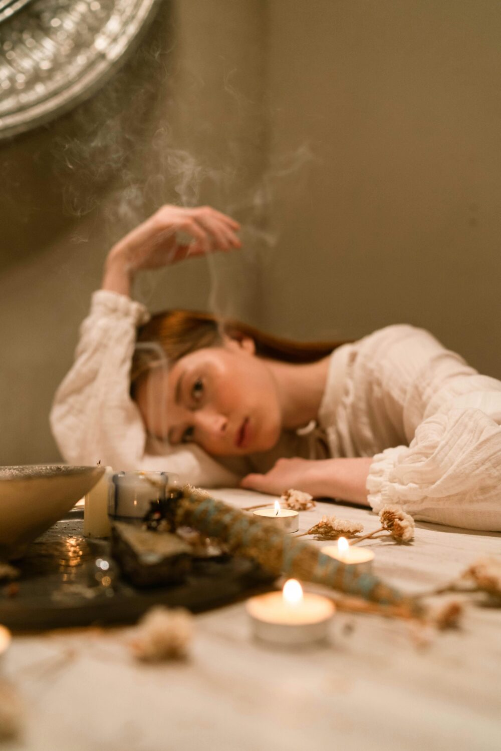 Person resting head on table with candles and dried flowers.