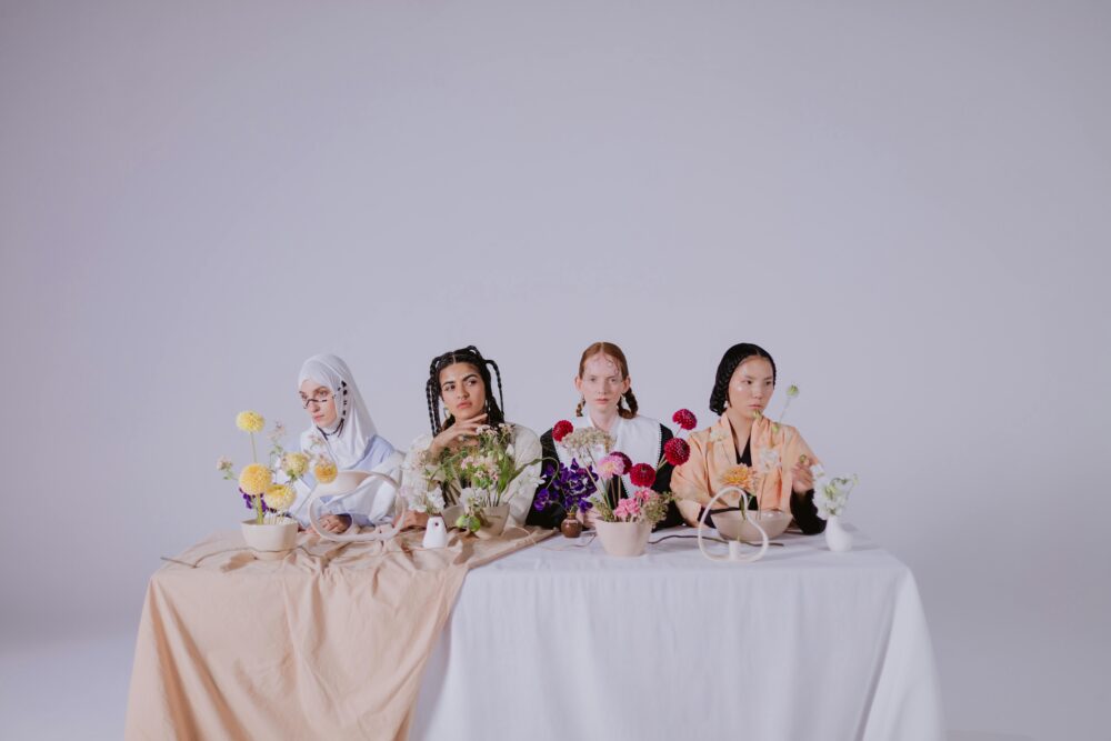 Four people sit at a table with flowers and bowls.