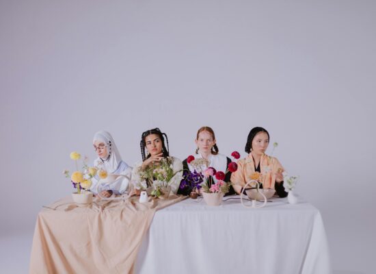 Four people sit at a table with flowers and bowls.