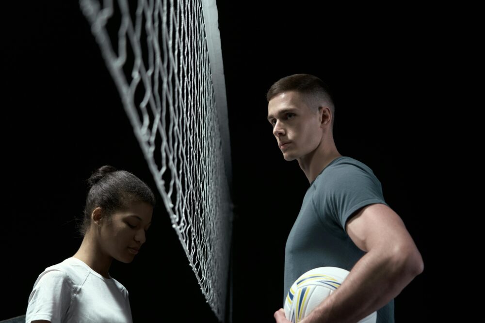 Two people stand on opposite sides of a volleyball net.