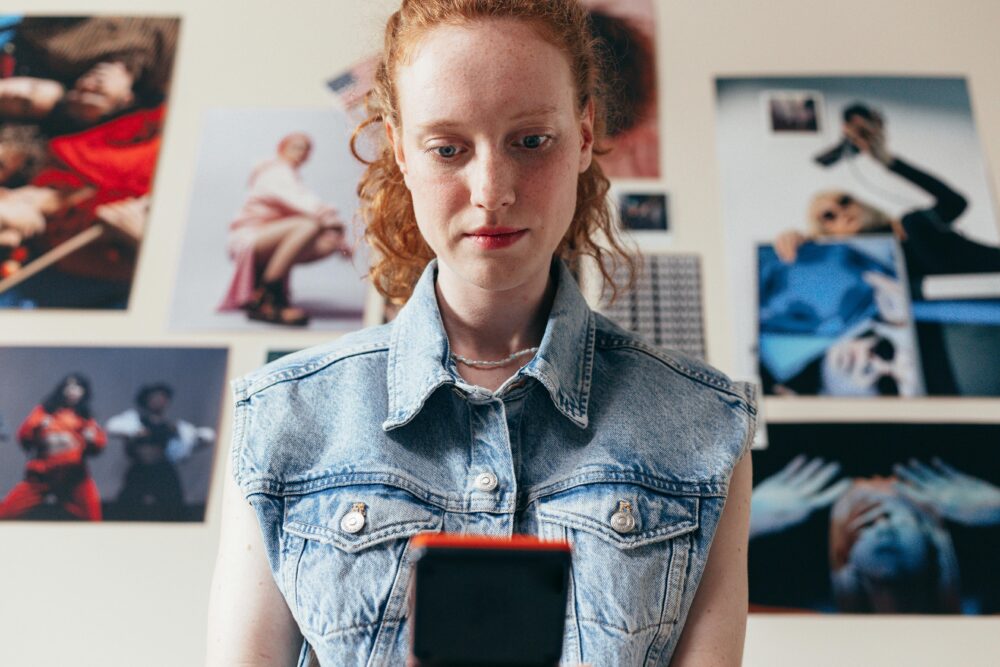 Person looking at phone with photos on wall behind them.