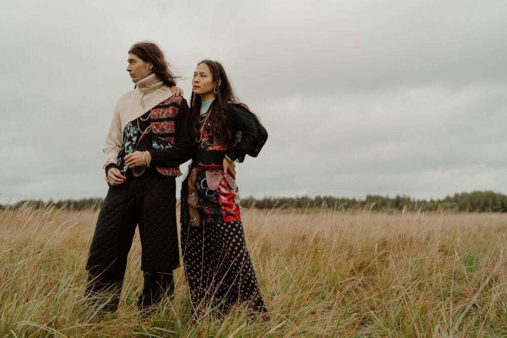 Two people stand in a field of tall grass under a cloudy sky.