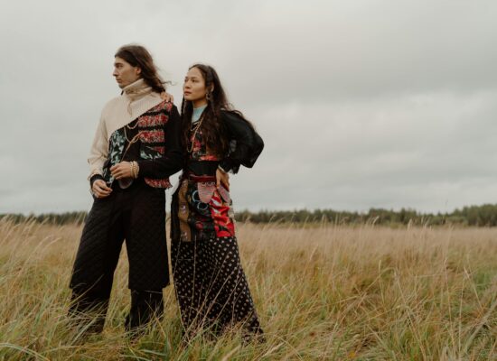 Two people stand in a field of tall grass under a cloudy sky.