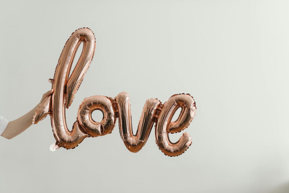 Rose gold balloon spelling 'love' held against plain background.