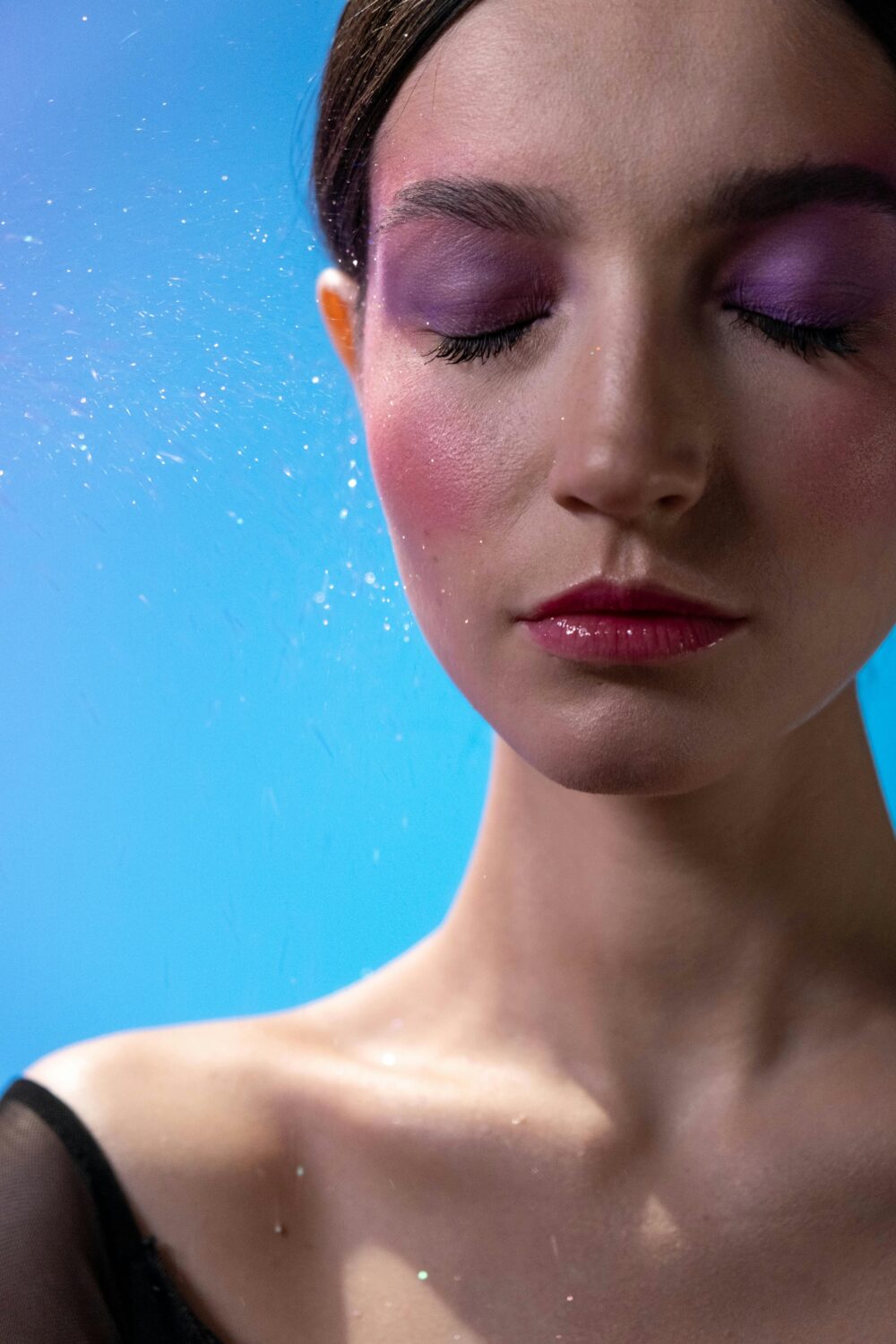 Person with closed eyes, colorful makeup, blue background, sparkles.