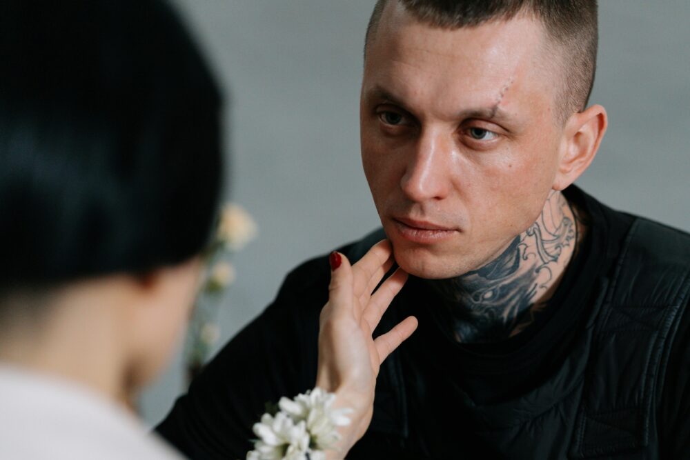 Person with tattoos being gently touched on the face, emotional moment.