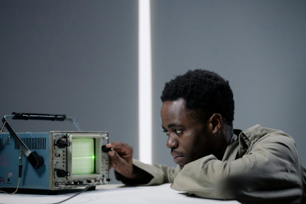 Person adjusting an oscilloscope, focused on the green display.