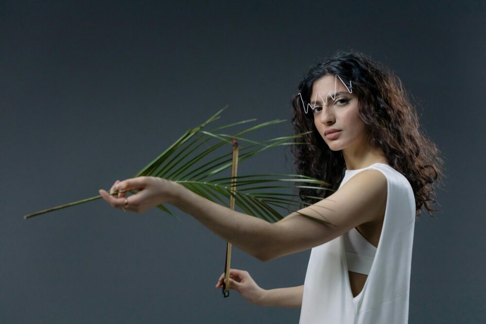 Person holding palm leaf, wearing white outfit, creative makeup.