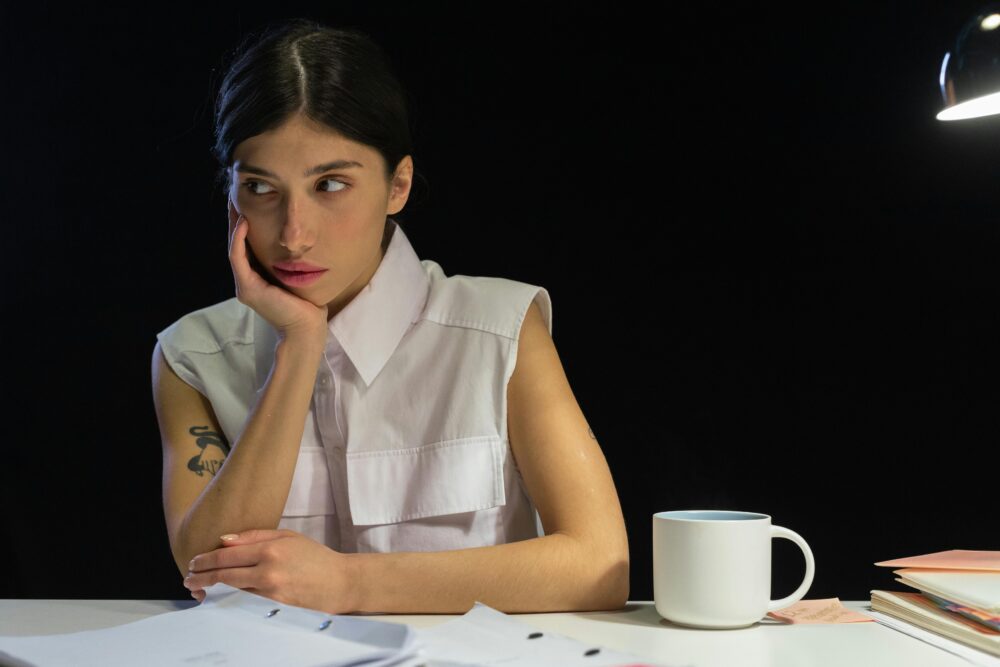 Person looking away from camera, resting chin on hand, with papers and mug.