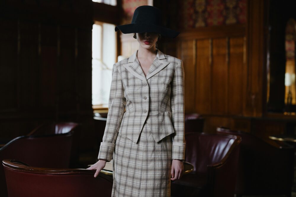 A person in a plaid suit and wide-brimmed hat stands in a dimly lit room.