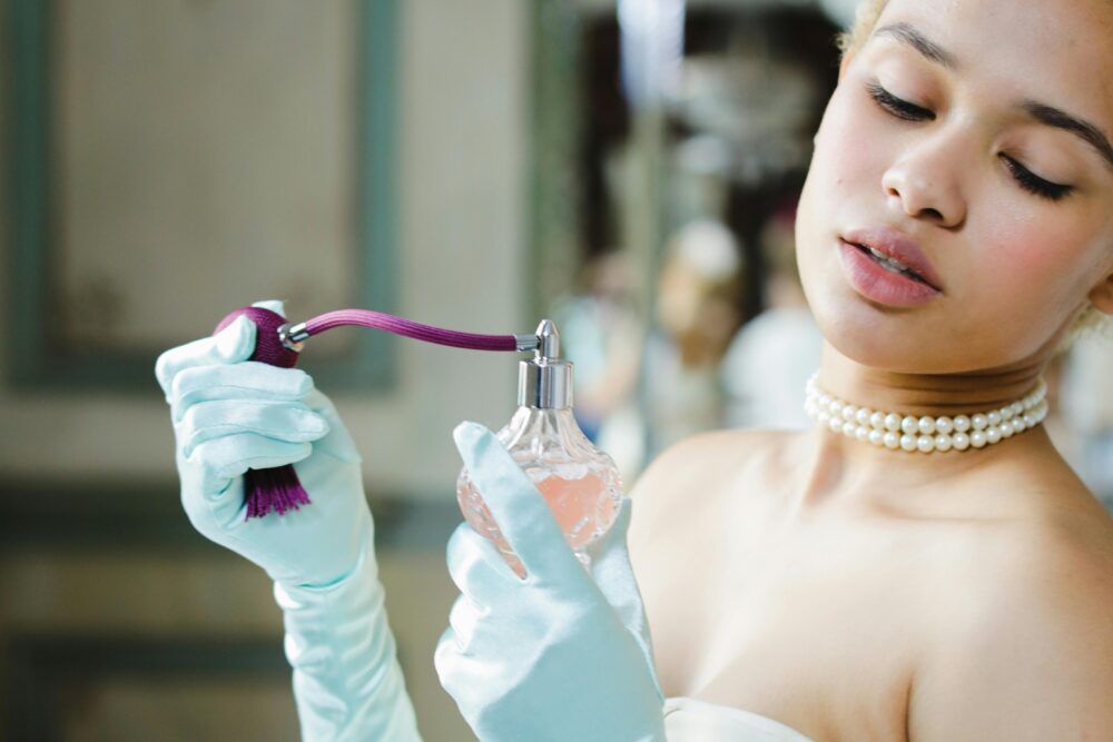 Person in light blue gloves sprays perfume from a vintage bottle.
