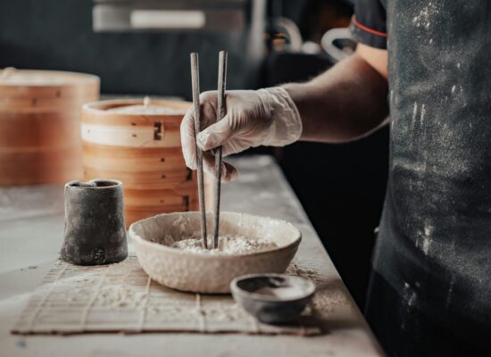 Gloved hand using chopsticks in flour, preparing food, kitchen scene.