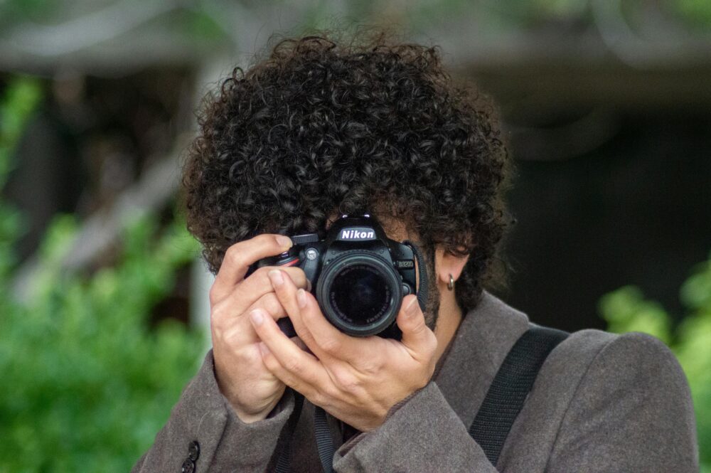 Person with curly hair taking a photo with a Nikon camera.