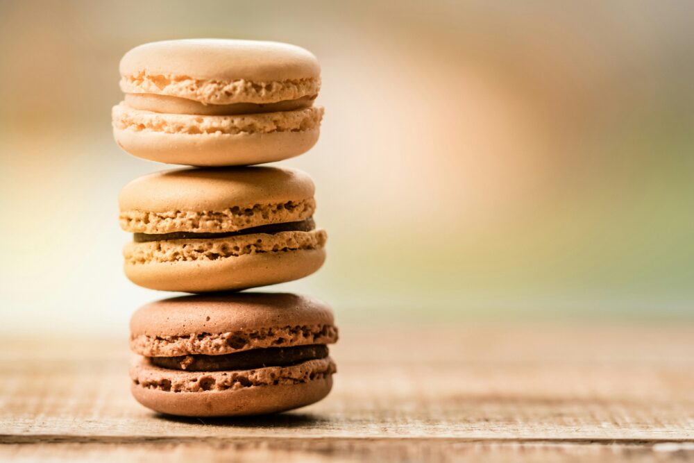 Three stacked macarons on a wooden surface, blurred background.