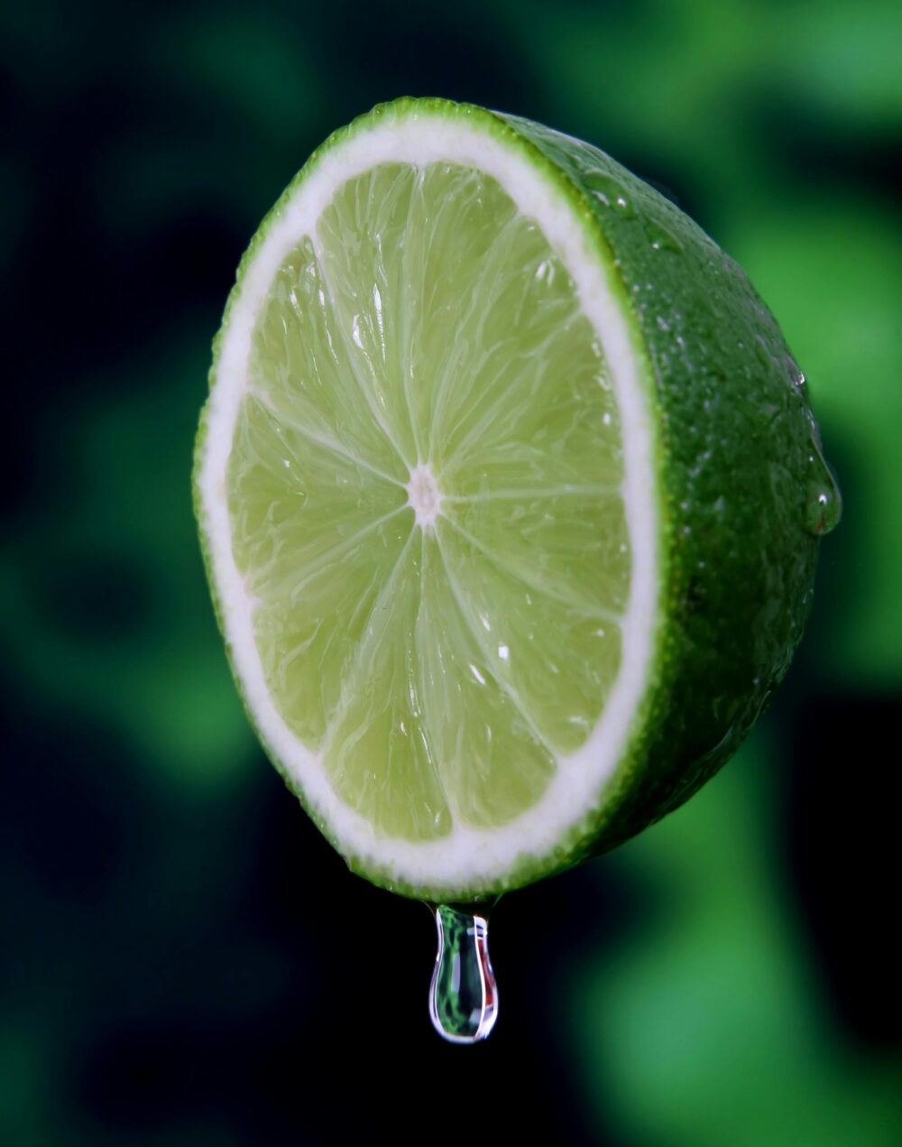 Close-up of lime slice with juice droplet, green background.