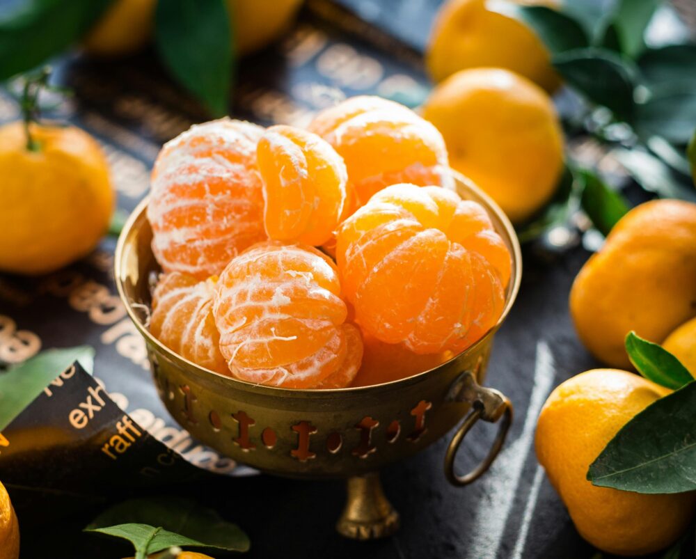 Peeled tangerines in a brass bowl surrounded by whole tangerines.