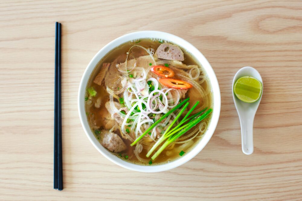 Bowl of Vietnamese pho with chopsticks, spoon, and lime wedge.