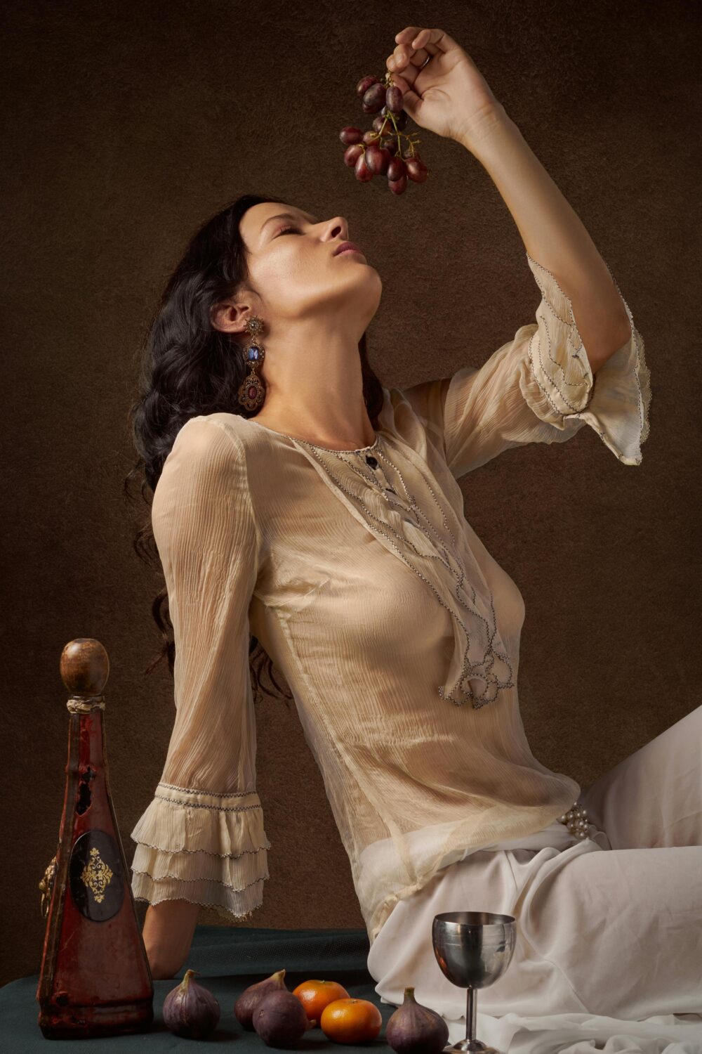 Person holding grapes, surrounded by fruit and elegant objects.