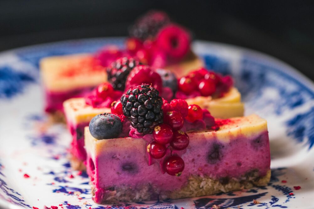 Colorful berry cheesecake slices on a decorative blue plate.