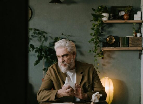 Person sitting at desk, holding tissue, surrounded by plants.