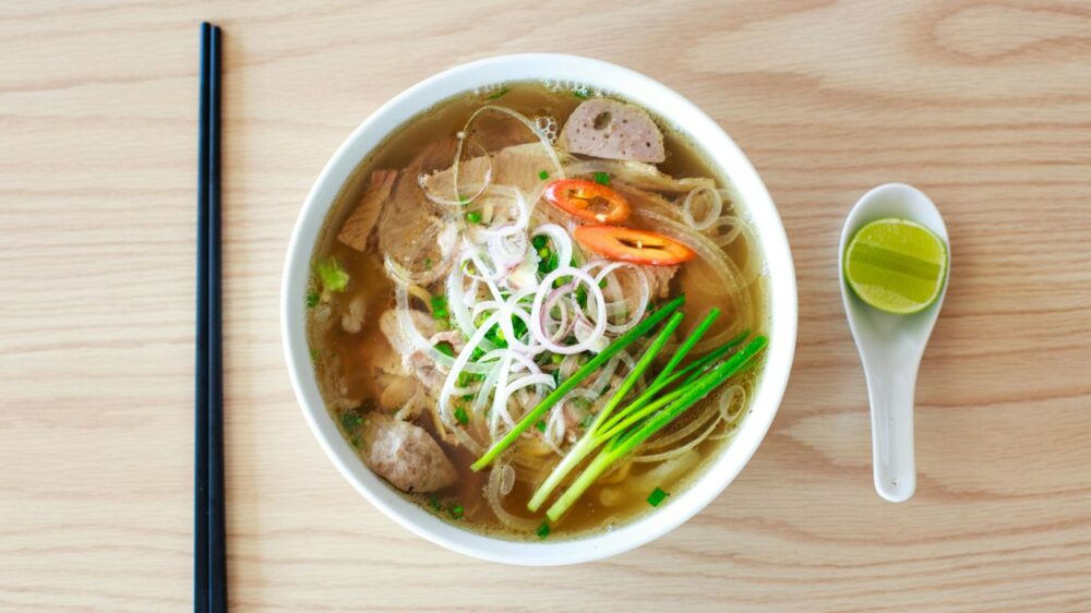 Bowl of Vietnamese pho with chopsticks, spoon, and lime wedge.