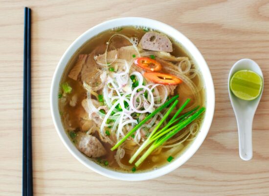 Bowl of Vietnamese pho with chopsticks, spoon, and lime wedge.
