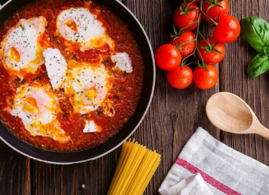Eggs in tomato sauce, fresh tomatoes, basil, pasta, wooden spoon.
